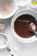 Chocolate cake batter in a white ceramic bowl, brownie batter in a mixing bowl