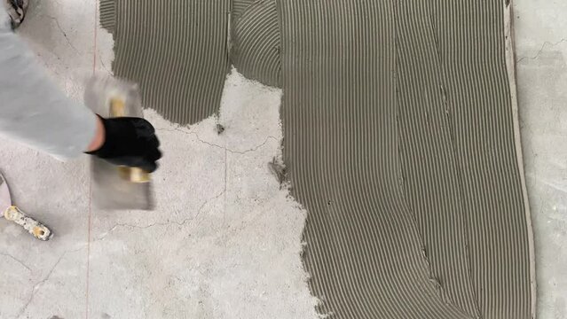 A builder applies tile adhesive to the floor. 4k video footage of construction work on laying tiles.