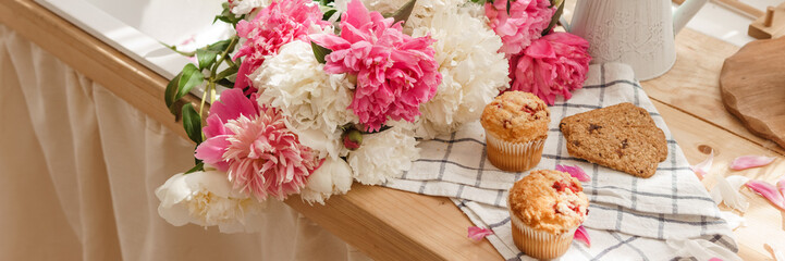 Fototapeta na wymiar The kitchen countertop is decorated with peonies. The interior is decorated with spring flowers. Pink peonies and sweet cupcakes on a wooden countertop. Interior details.