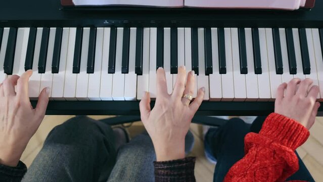 A Teacher Teaches A Child To Play The Piano. Close-up Of The Hands Of A Teacher And A Child Playing The Piano, Pressing The Keys With Their Fingers, Top View.