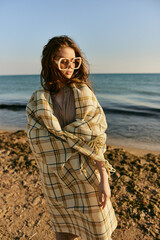 cute woman stands with a plaid during sunset on the beach. Rest, enjoyment