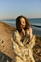 portrait of a woman in a blanket standing on the shore and straightening her hair flying in the wind