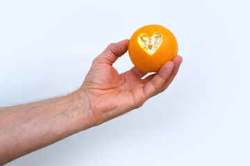 male hand holds, offers orange, beautiful composition with heart carved in citrus, concept of love, vitamins, healthy eating, healthy life, idea for design for Valentine's Day, Mother's Day, wedding