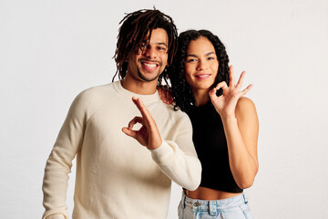 A Latin couple making the ok symbol with their hands looking at the camera in a studio shot - 565320667