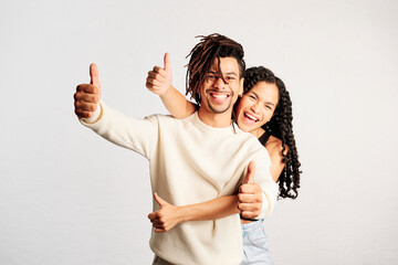 A cheerful young woman behind her cheerful boyfriend making two thumbs-up with hands in a studio - 565320695