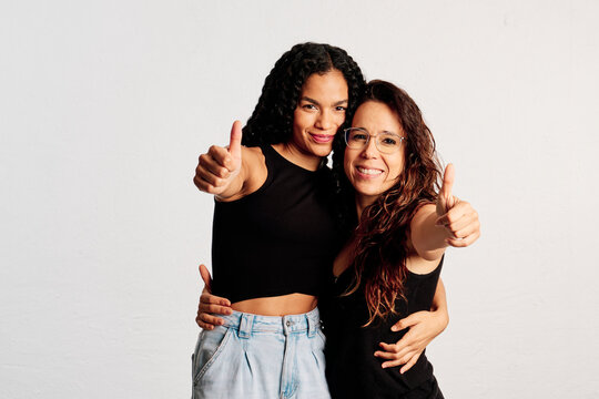 Two close friends showing their thumbs up to the camera while smiling at a studio shot