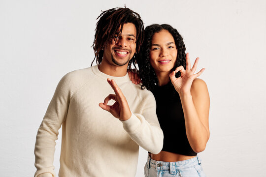 A Latin couple making the ok symbol with their hands looking at the camera in a studio shot