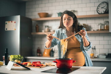 Beautiful pregnant woman preparing delicious food. Smiling woman cooking at home..