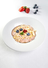 Oatmeal with almonds, blueberries and strawberries in a white plate on a white background