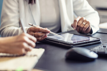 The hands of two female colleagues are using a digital tablet and a notebook. A business meeting to...