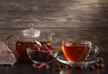 A cup of brewed berry tea and dried rose hips on a wooden table