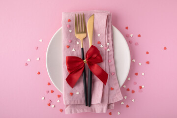 Valentine's Day background. A set of golden cutlery and pink napkin on plate with hearts confetti