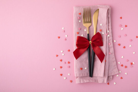 Valentine's Day background. A set of golden cutlery and pink napkin with hearts confetti