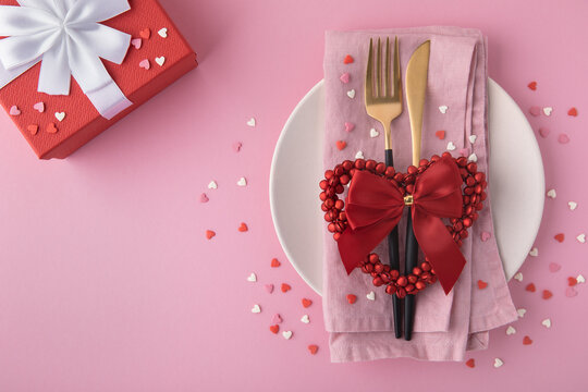 Valentine's Day background. A set of golden cutlery and pink napkin on plate with hearts confetti