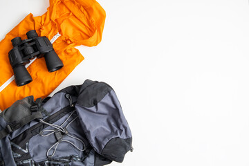 Binoculars, tourist backpack, raincoat on a white background. Top view, flat lay