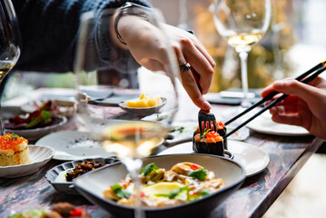 woman hand eating food in restaurant. wine, cheese, meat, vegetables and other appetizers on table
