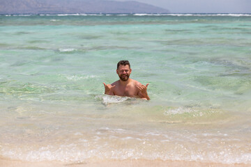 Young caucasian bearded man having fun in bright blue oceanic water, enjoying his holidays at Bali Indonesia