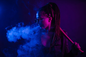 A young woman with dreadlocks smokes a cigarette in a club. Wearing black glasses, he holds a...