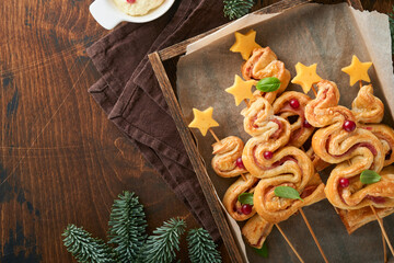 Christmas or New Year appetizer. Christmas tree shape puff pastry buns with cheese and ham. Group of Christmas tree shapes on wooden board. Festive idea for Christmas or New Year dinner. Top view.