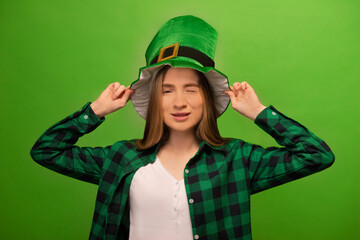 Naklejka premium Winking young woman wearing leprechaun hat and green checkered plaid shirt with white shirt isolated on colorful green background.St Patricks Day celebration and holiday concept.
