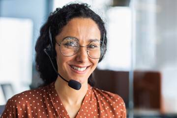 Close-up photo. Portrait of a young beautiful Latin American woman in a headset. Call center, service operator, hospital reception, support and assistance line. He looks at the camera, smiles.