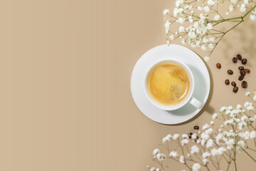 Coffee composition with cup of natural coffee and coffee beans on beige background with white flowers and copy space. Spring morning composition with cup of fresh hot espresso. Breakfast. Flat lay