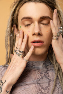 Portrait of young queer person with dreadlocks touching face isolated on yellow.