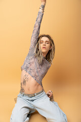 Tattooed queer person in crop top with animal print posing on yellow background.