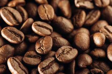 Roasted coffee beans background. Many aromatic coffee beans on a dark background. Selective focus. Close-up. The concept of an advertising banner for a coffee shop or chain of commodity production.