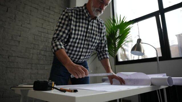 Mature architect or engineer open blueprint on the desk in office. Architect working in office