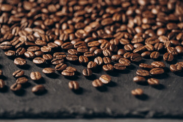 Roasted coffee beans background. Many aromatic coffee beans on a dark background. Selective focus. The concept of an advertising banner for a coffee shop or chain of commodity production.