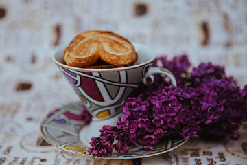 a cup with cookies stands next to a purple lilac 