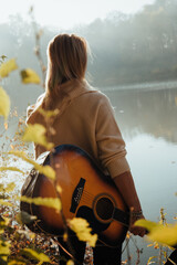 a girl stands with a guitar near the river 