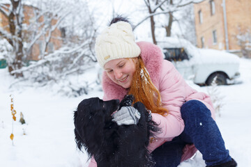 a girl plays with a black cocker spaniel in the winter