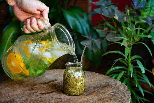 mano cebando terer&eacute;, bebida t&iacute;pica de argentina y paraguay. bebida fr&iacute;a con hielo, lim&oacute;n y hojas de menta. mesa de madera r&uacute;stica y entorno natural.