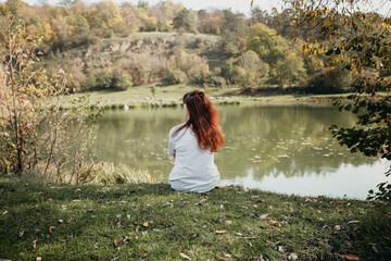 a girl with loose hair sits on the bank of the river 