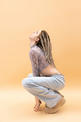 Side view of queer person in crop top with snakeskin print and jeans looking up on yellow background.