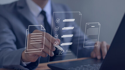 Businessman using pen to sign electronic documents with virtual screen on laptop computer on table...