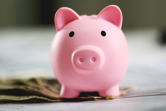 Um cofrinho com notas de D&oacute;lares dos Estados Unidos sobre uma mesa de madeira. Conceito de guardar dinheiro e investimentos.	