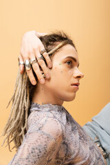 Stylish nonbinary person with silver rings on fingers isolated on yellow.