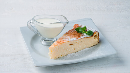 Piece of cheesecake with mint, powdered sugar and vanilla sauce.