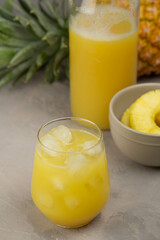 Pineapple juice in a clear glass and bottle on a light table. Pineapple and slices in the background.
