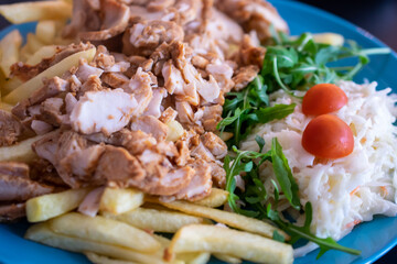 kebab with potato fries and salad on a blue plate