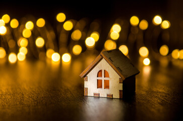 One small wooden toy house on black background, illuminated from the side and behind by round yellow blurred lights