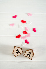 Two small wooden houses on white background, pink hearts between them, concept of family happiness, buying a house