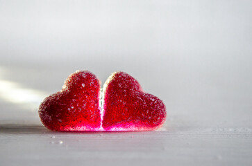 Two red sugar marmalade candies in the shape of heart on a white background, lit from the side, with copyspace