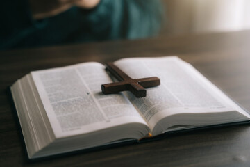 Naklejka premium Close up of an open bible with a cross for morning devotion on a wooden table with window lights.