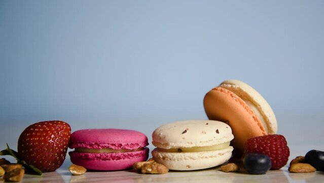 A girl's hand puts macarons in the frame, the photographer lays out a composition of French desserts and fruits on a blue photo.