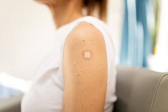 Close up shot of a woman's arm with a circular band aid from a shot