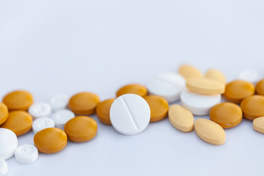 Orange and white medical tablets scattered on white with copy space